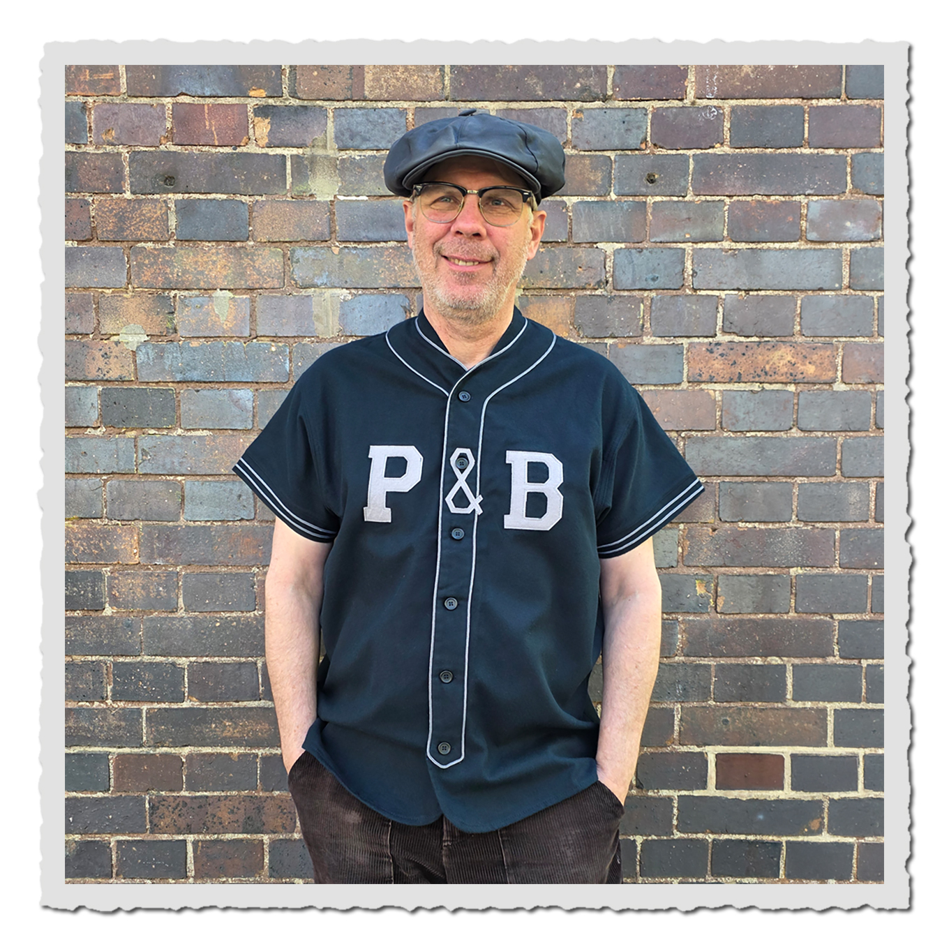 Person von vorn im dunkelblauen Baseballshirt vor gemauerter Backsteinwand im Außenbereich.